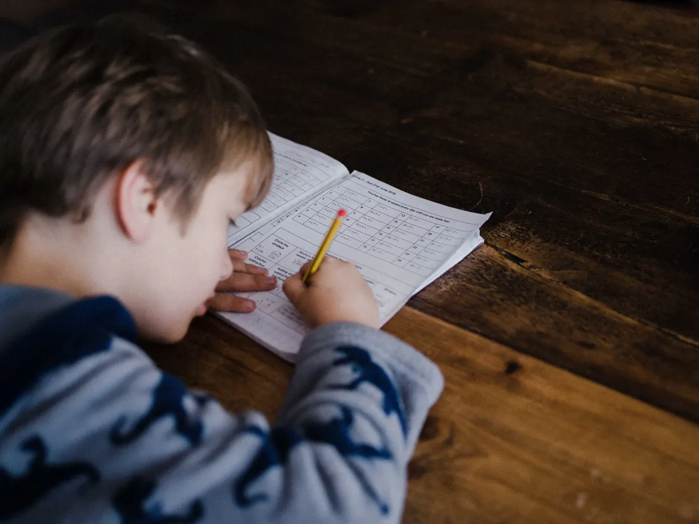 A child working through handwritten arithmetic exercises at a table